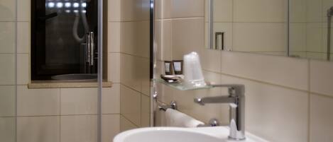 Un baño moderno con ducha de vidrio, lavamanos blanco y un espejo.