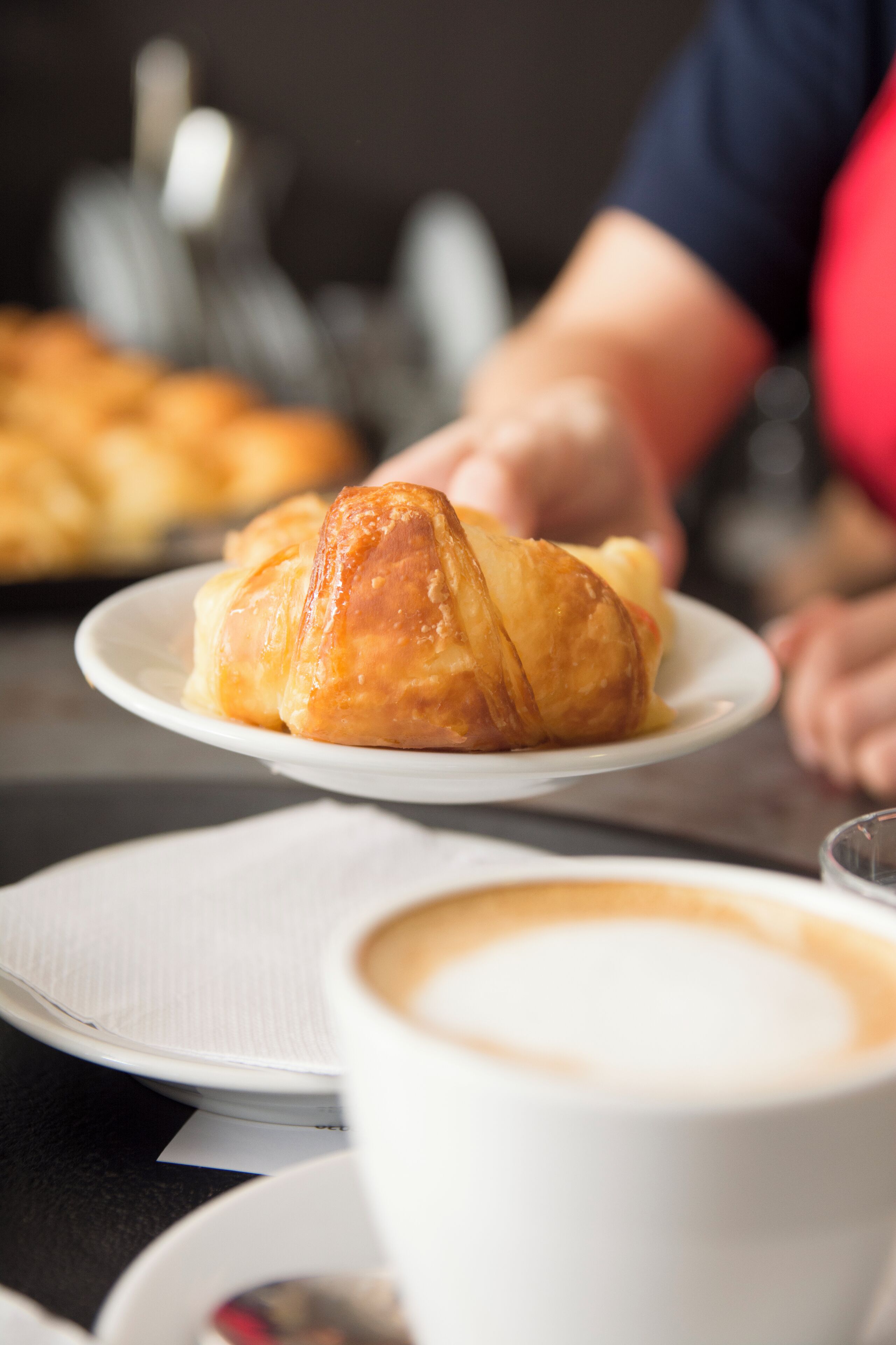 A croissant on a plate with a cup of coffee in the foreground.