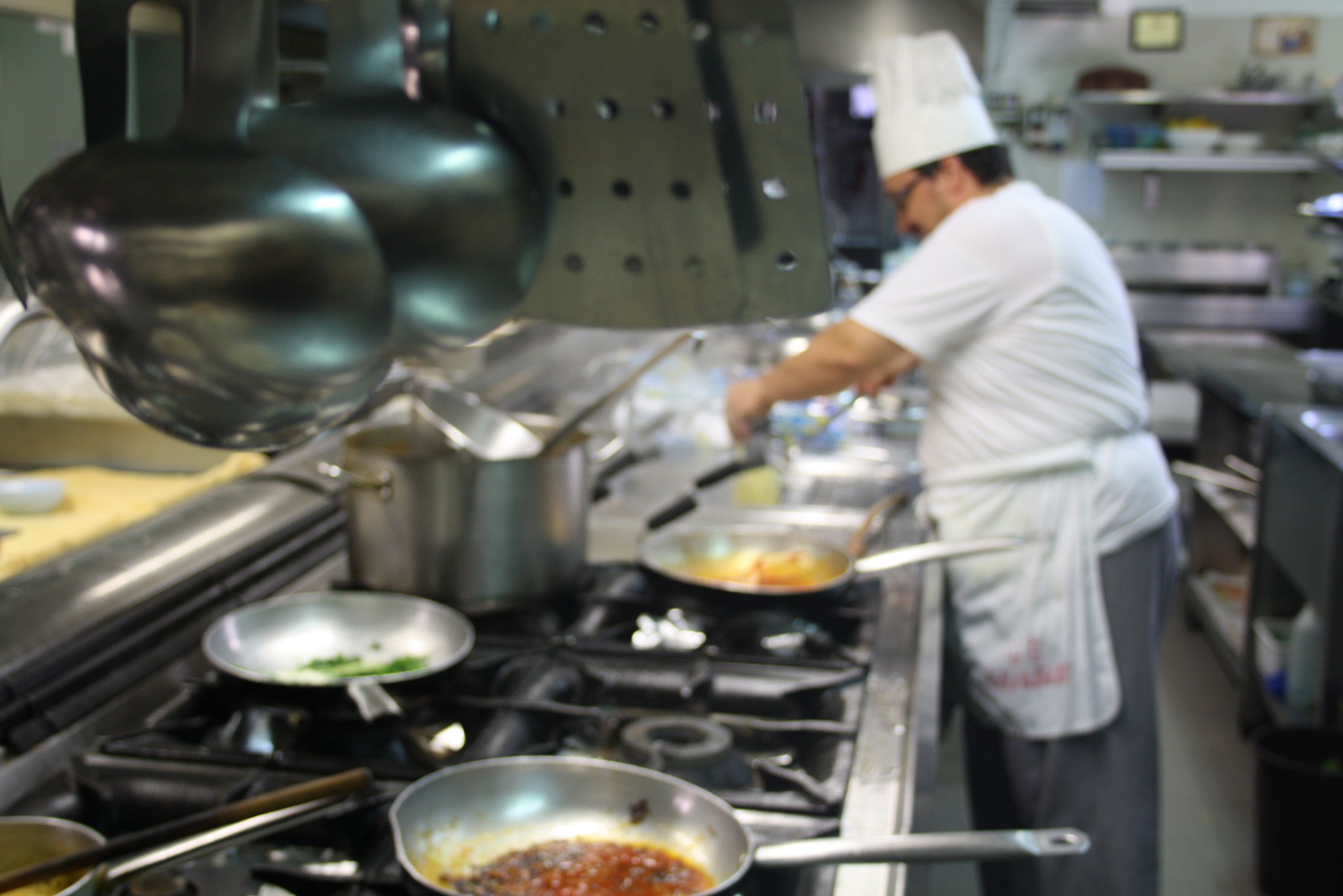 A chef in a kitchen with stainless steel appliances and cookware.