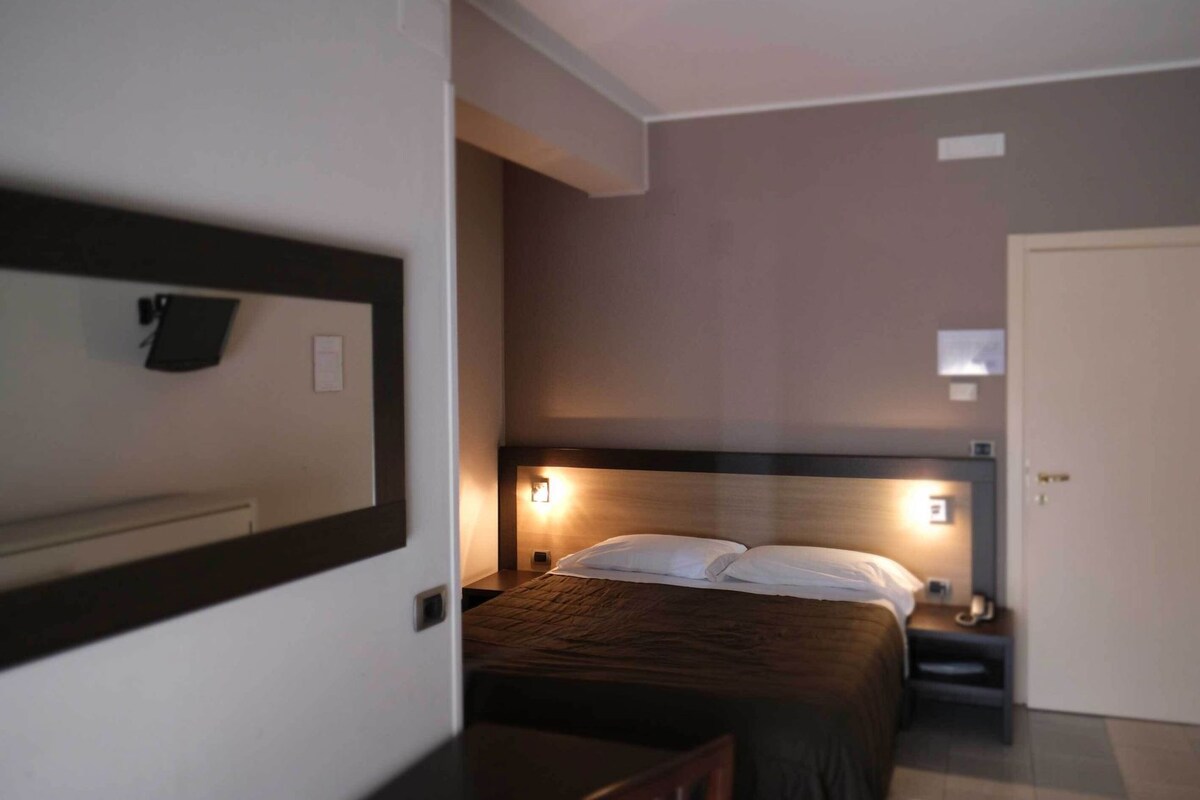 Una habitación de hotel con cama, mesita de noche y puerta.