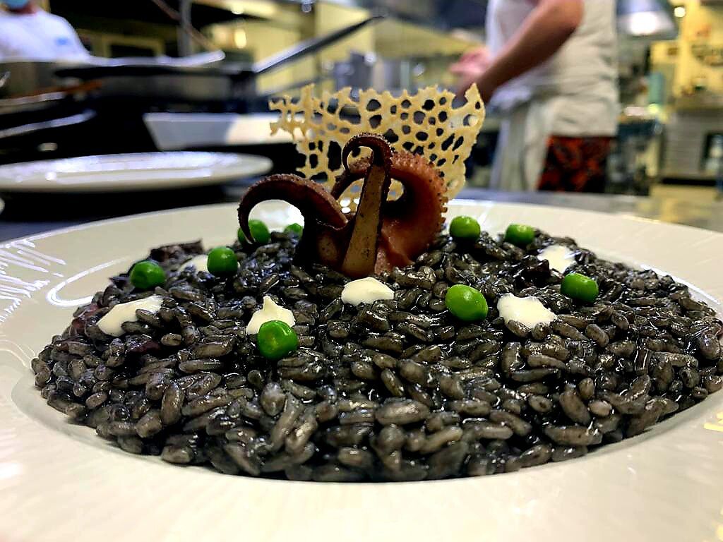Un plato de risotto negro adornado con guisantes y un detalle decorativo.