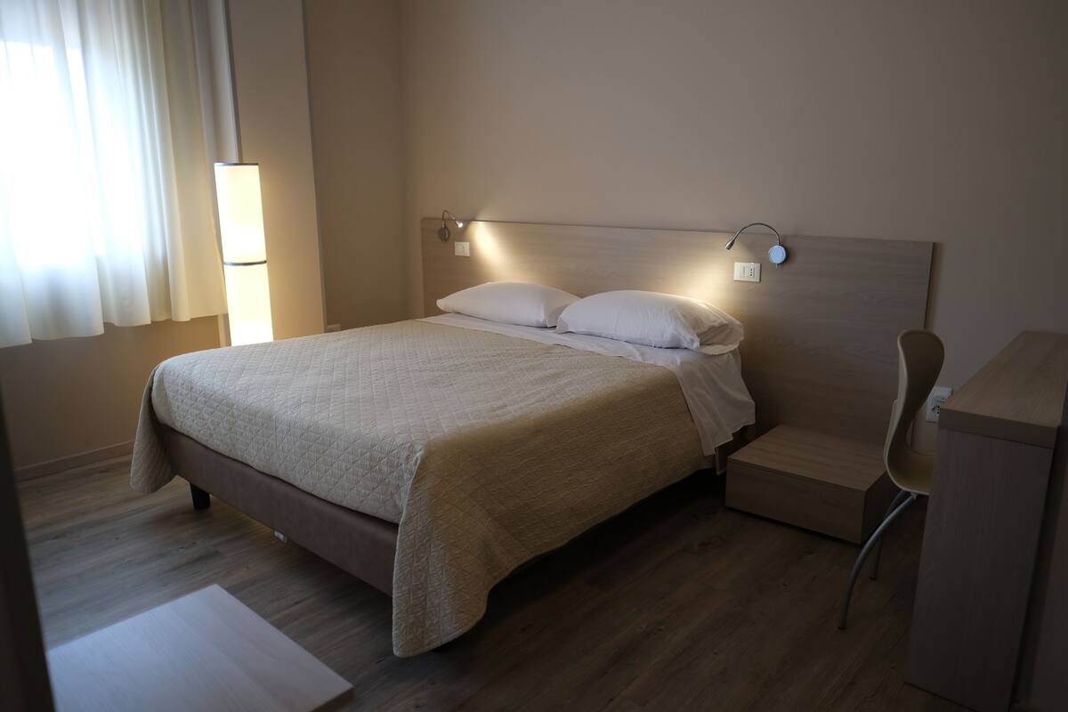 Una cama bien hecha, con cabecera, mesita de noche y una silla.