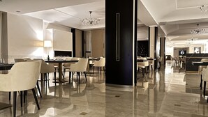 Un moderno vestíbulo de hotel con suelo de mármol, mesas y sillas para comer. Se observan candelabros y una chimenea.