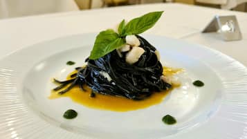 Prato de massa preta com um toque de manjericão e um pouco de creme, servido em prato branco com molho amarelo e pontos verdes.