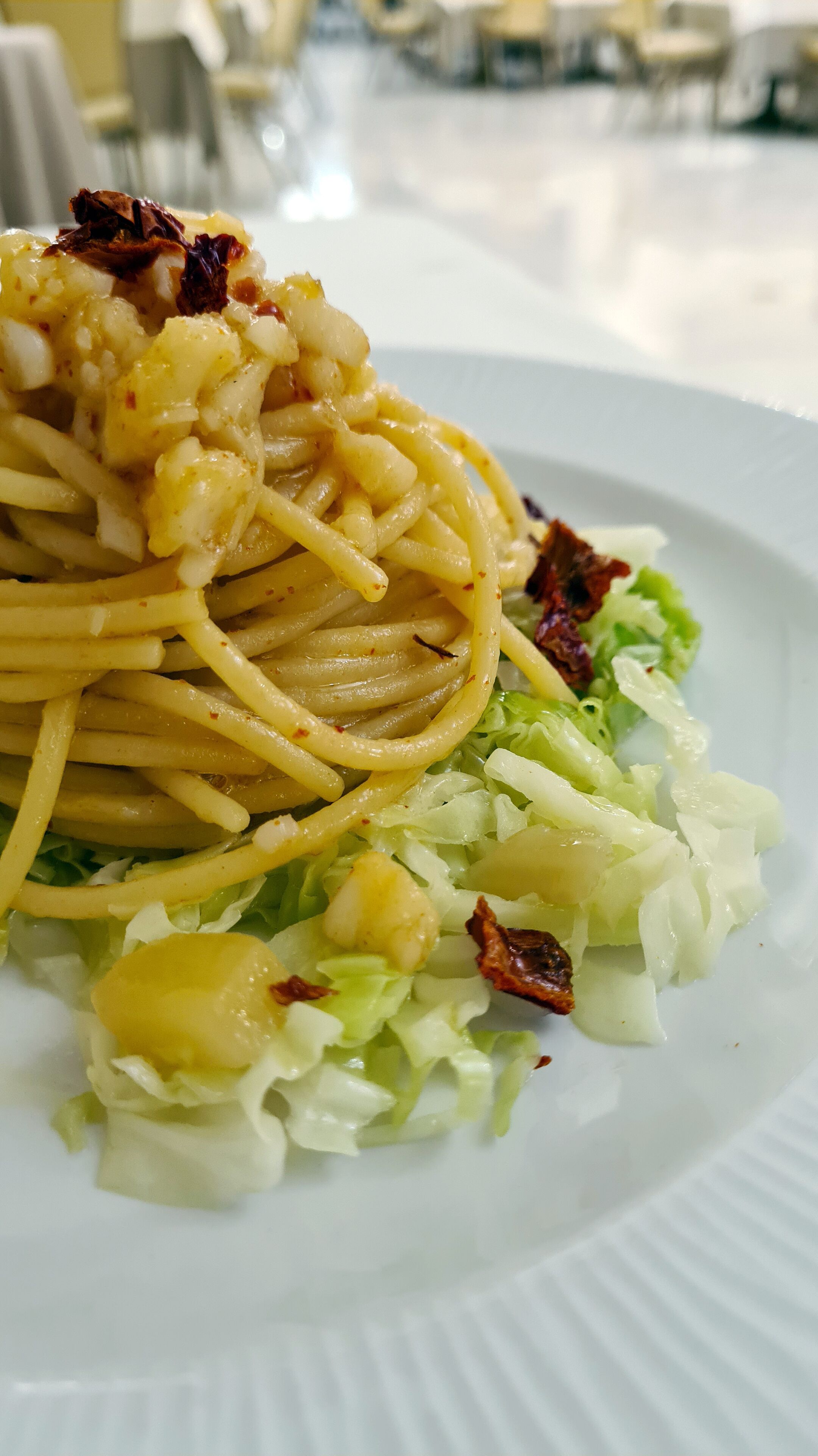 Un plato de espagueti acompañado de ensalada mixta y crujientes trozos de tocino.