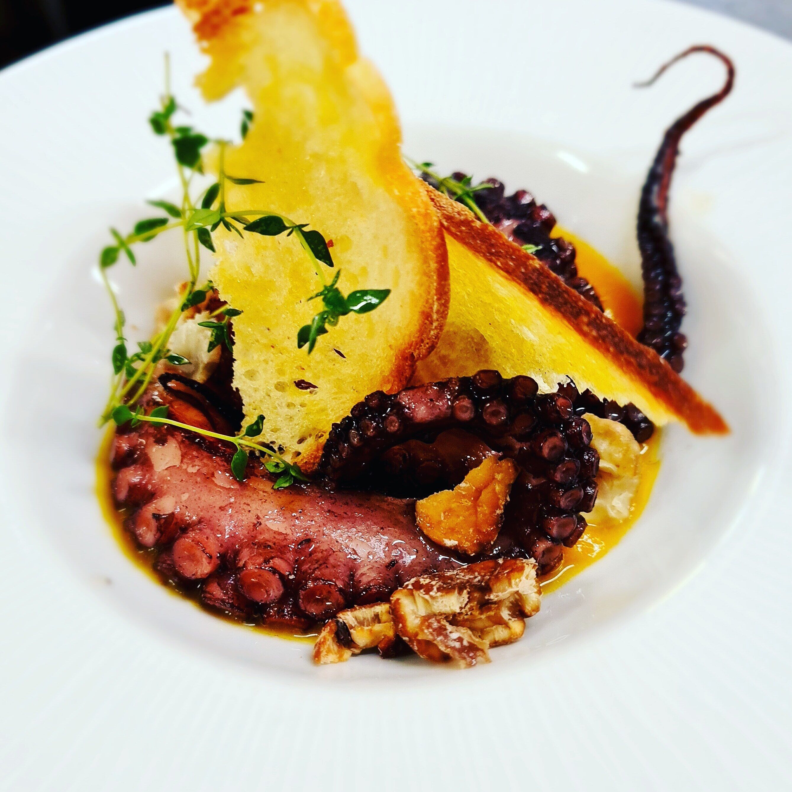 Een bord met octopus, brood en garnering.