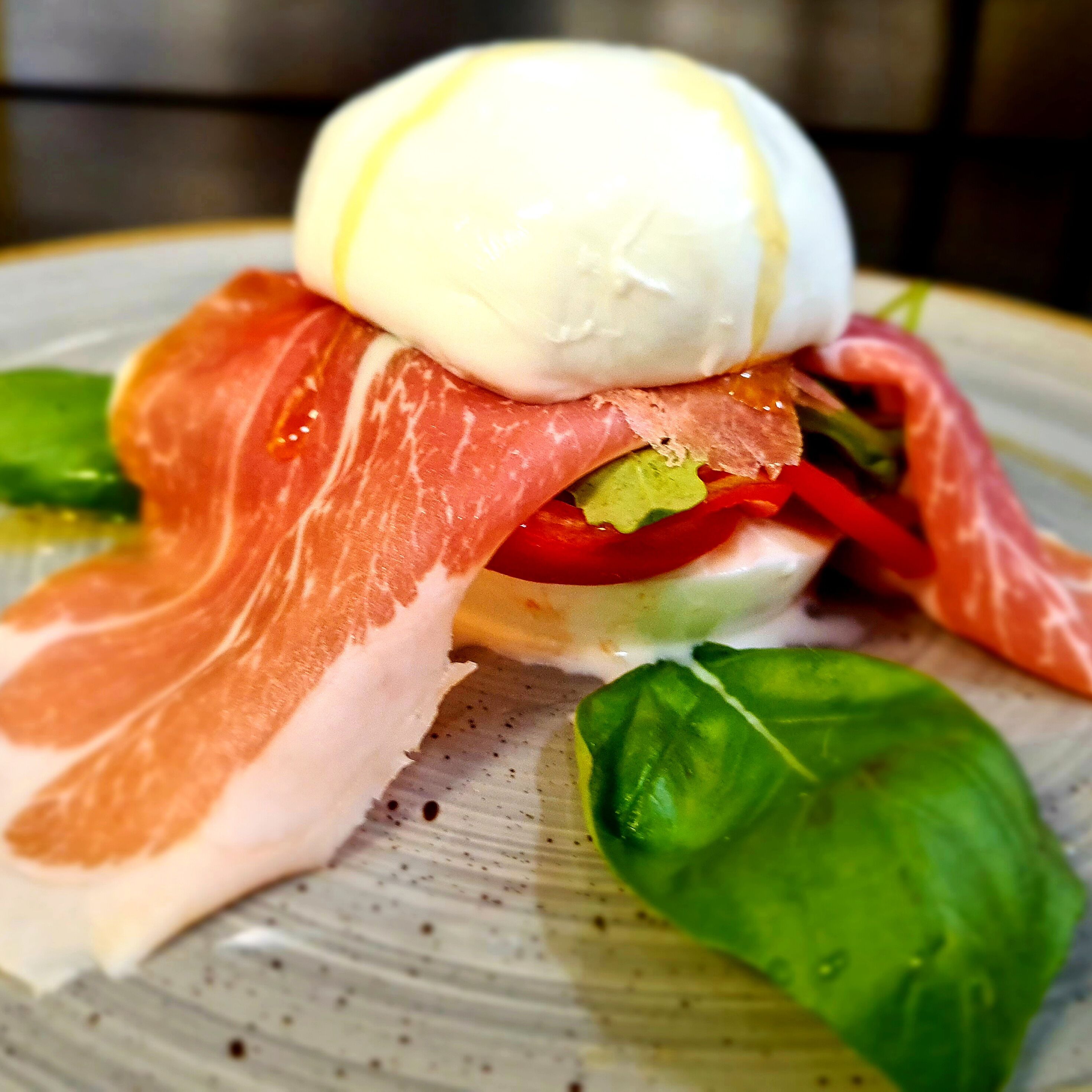 A plate with a sandwich, including a slice of ham, a slice of cheese, and a ball of mozzarella cheese.