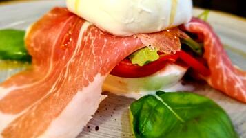 A plate with a sandwich, including a slice of ham, a slice of cheese, and a ball of mozzarella cheese.