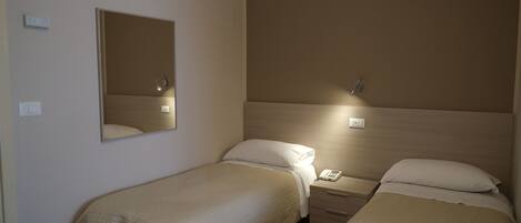 Una habitación de hotel con dos camas individuales, una mesita de noche con lámpara, un espejo y un enchufe.
