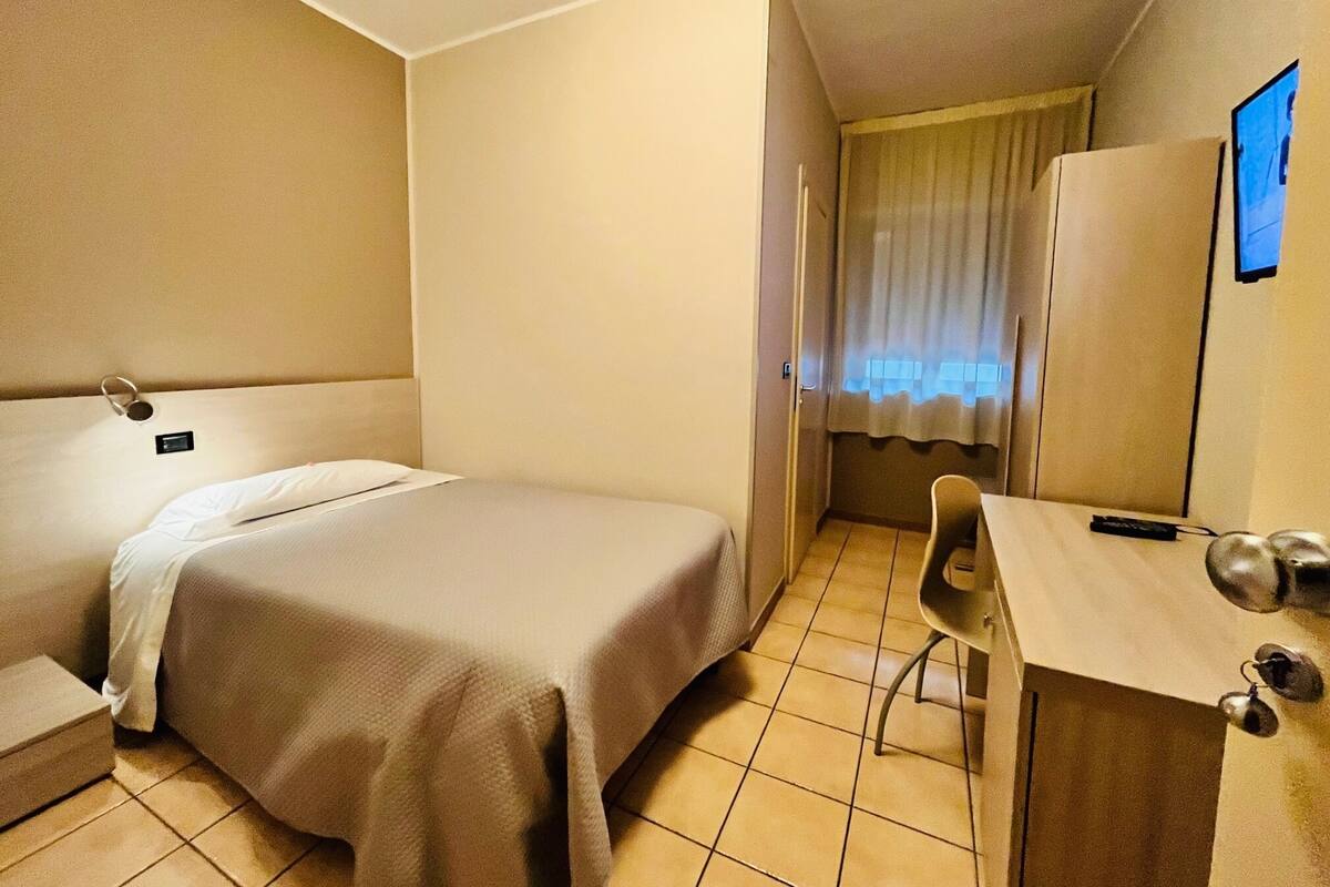 Habitación de hotel con cama, escritorio, silla, televisión y ventana con cortinas.