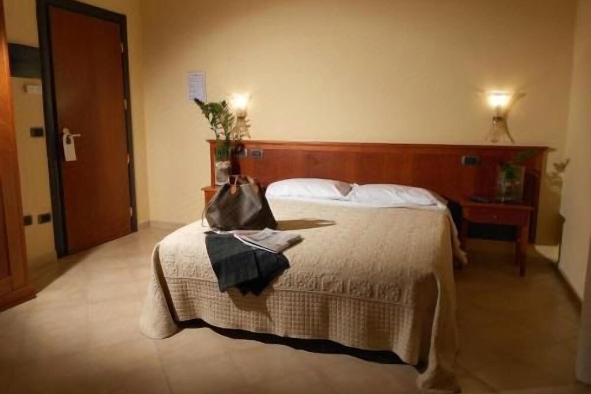Una habitación de hotel con una cama, una mesita de noche, una lámpara y una puerta.