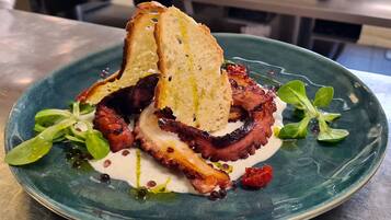 A plate with grilled octopus, toasted bread, and greens.