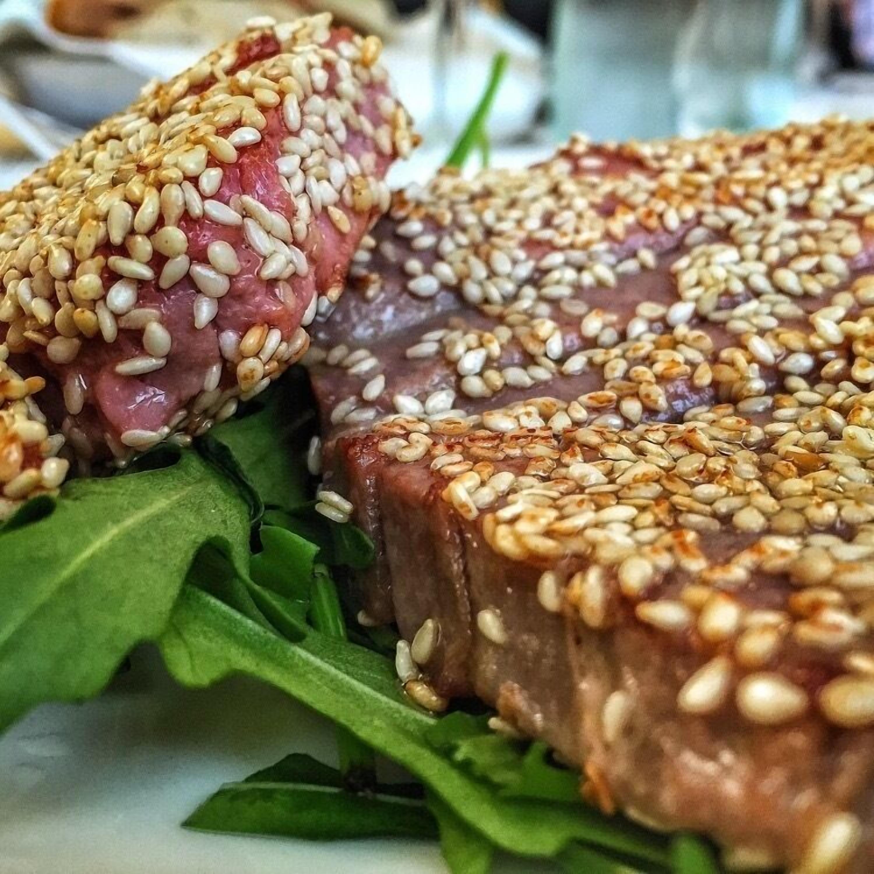 A close-up of a dish with sesame seeds on top, accompanied by green leafy vegetables.