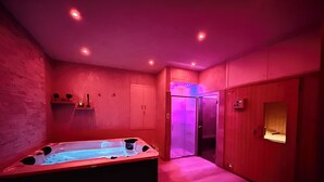 Una habitación con bañera de hidromasaje, armarios de madera, una puerta con ventanal e iluminación empotrada en el techo.