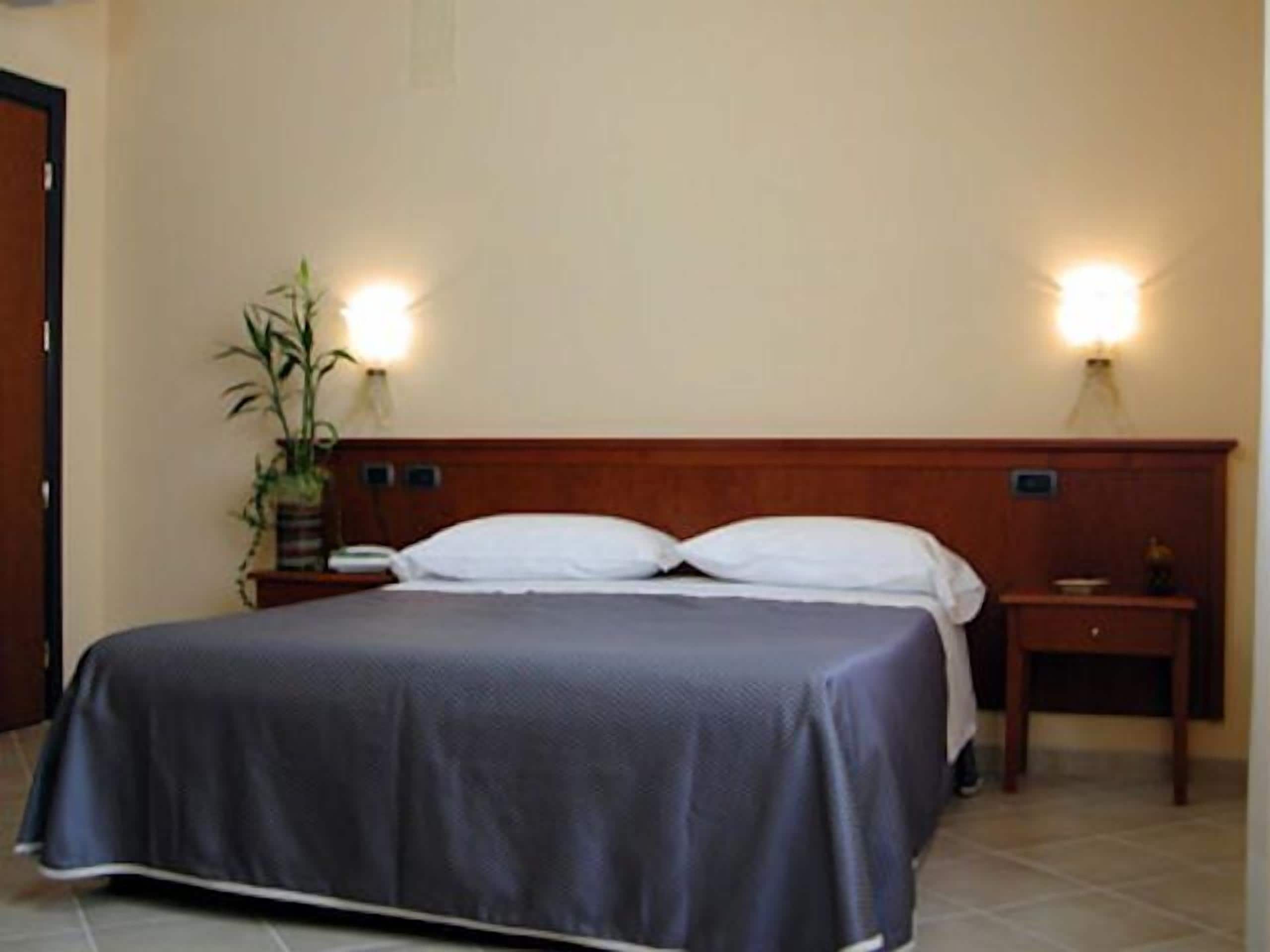Una camera d'albergo con un letto, due comodini e luci a parete.