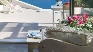 A balcony with a view of a cliff and sea, a bottle of wine, a glass, and a table with magazines and flowers. - Aura Marina Apartments Santorini (Santorini)