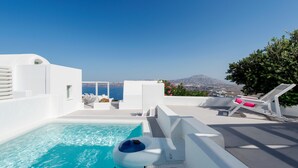 A pool area with clear blue water, white walls, and a view of the sea and a mountain in the background. - Aura Marina Apartments Santorini (Santorini)