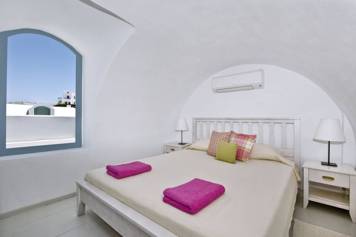Une chambre à coucher comprenant un lit, deux tables de chevet, une fenêtre et un appareil de climatisation.