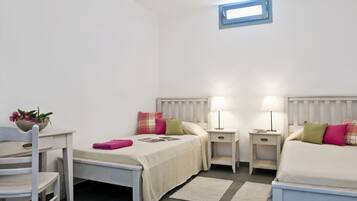 Una habitación pequeña y limpia con dos camas, un escritorio y una silla. Se ve el cielo por la ventana.