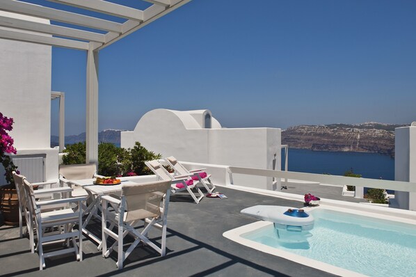 A rooftop terrace with white furniture, a pool, and a view of the sea.