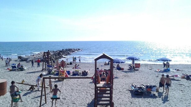 A beach with a lifeguard tower, umbrellas, and people relaxing. - Le Dune (Castel Volturno)
