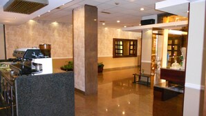 A lobby with a coffee machine, a reception desk, a mirror, and a plant. - Le Dune (Castel Volturno)