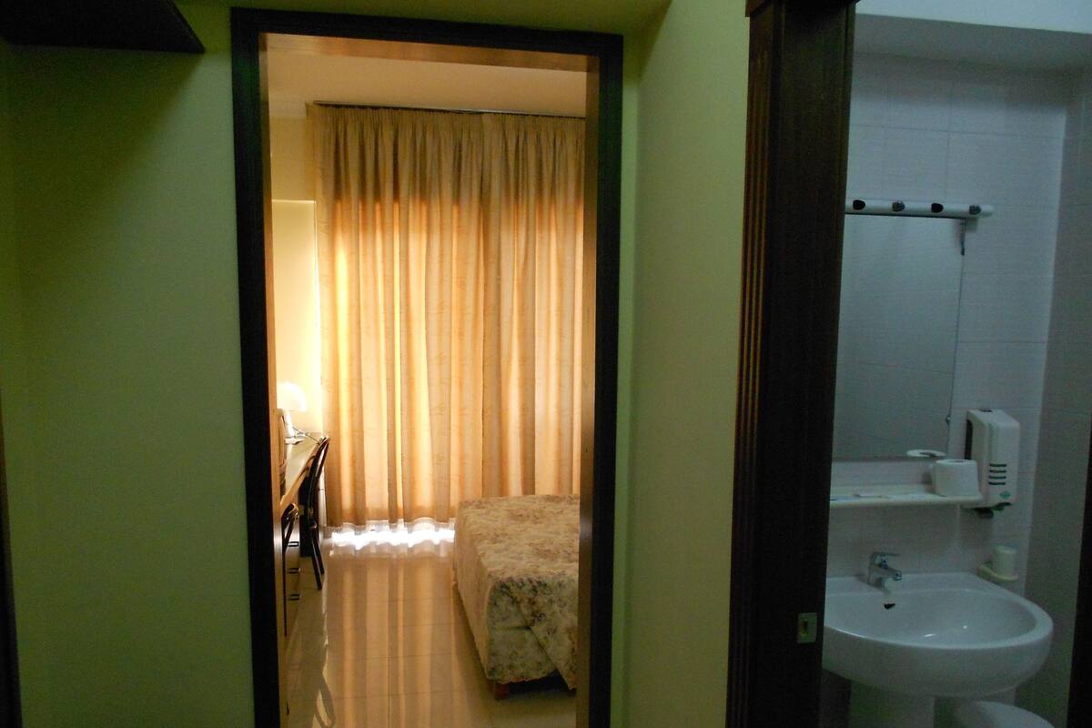 A hotel room with a bed, a bathroom with a sink and mirror, and a curtain-covered window.