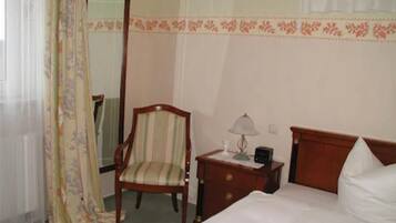 Habitación de hotel con cama, una silla, una mesita de noche con lámpara y un espejo.