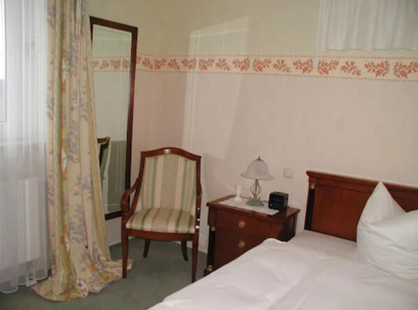 A hotel room with a bed, a chair, a nightstand with a lamp, and a mirror.