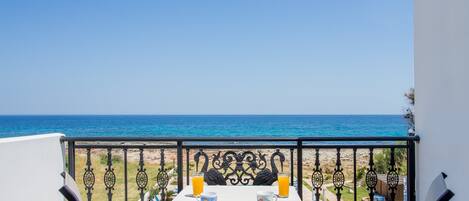 A balcony with a table set for two, overlooking a beach and the sea.