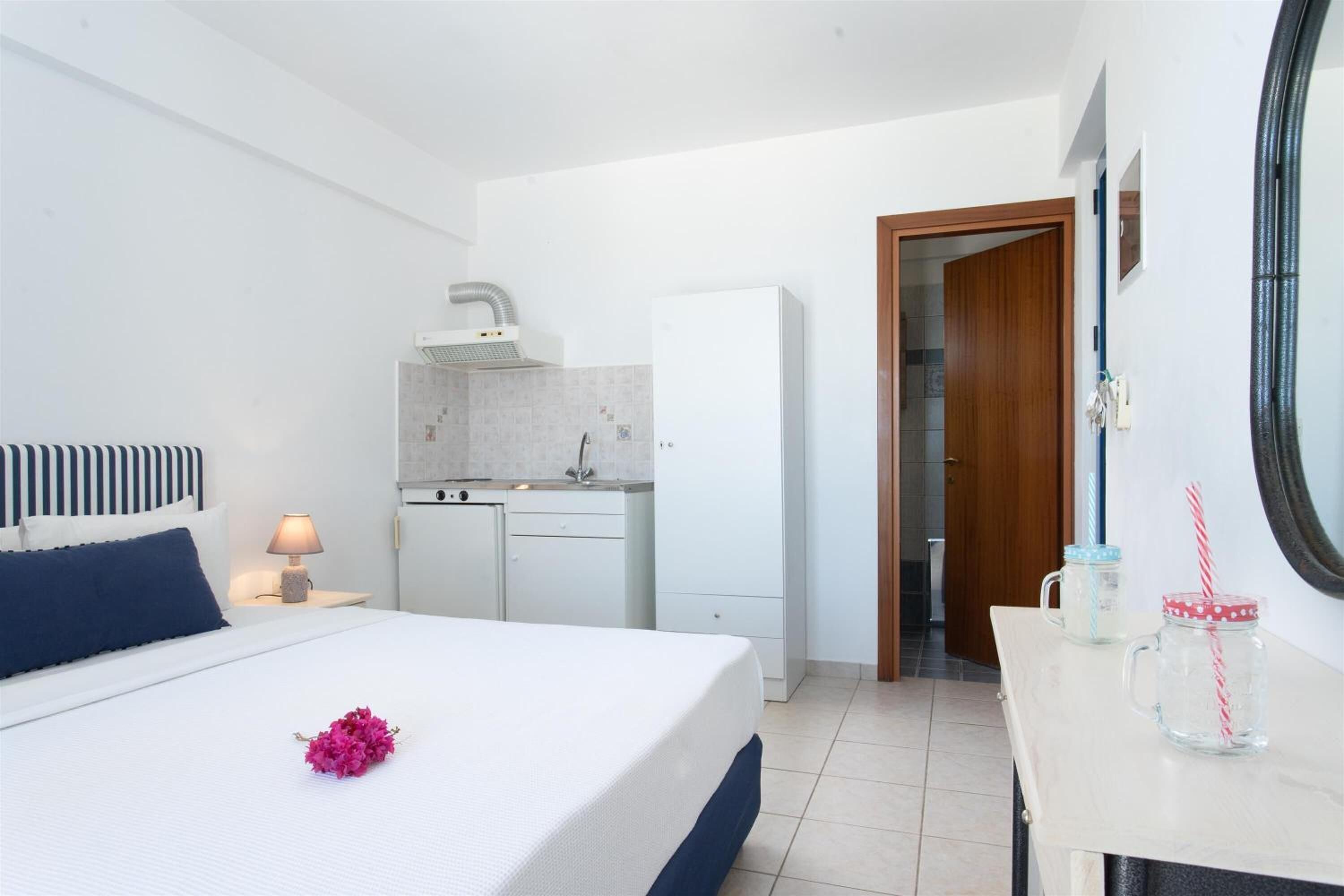 Habitación de hotel pequeña con cama, mesita de noche y una kitchenette.