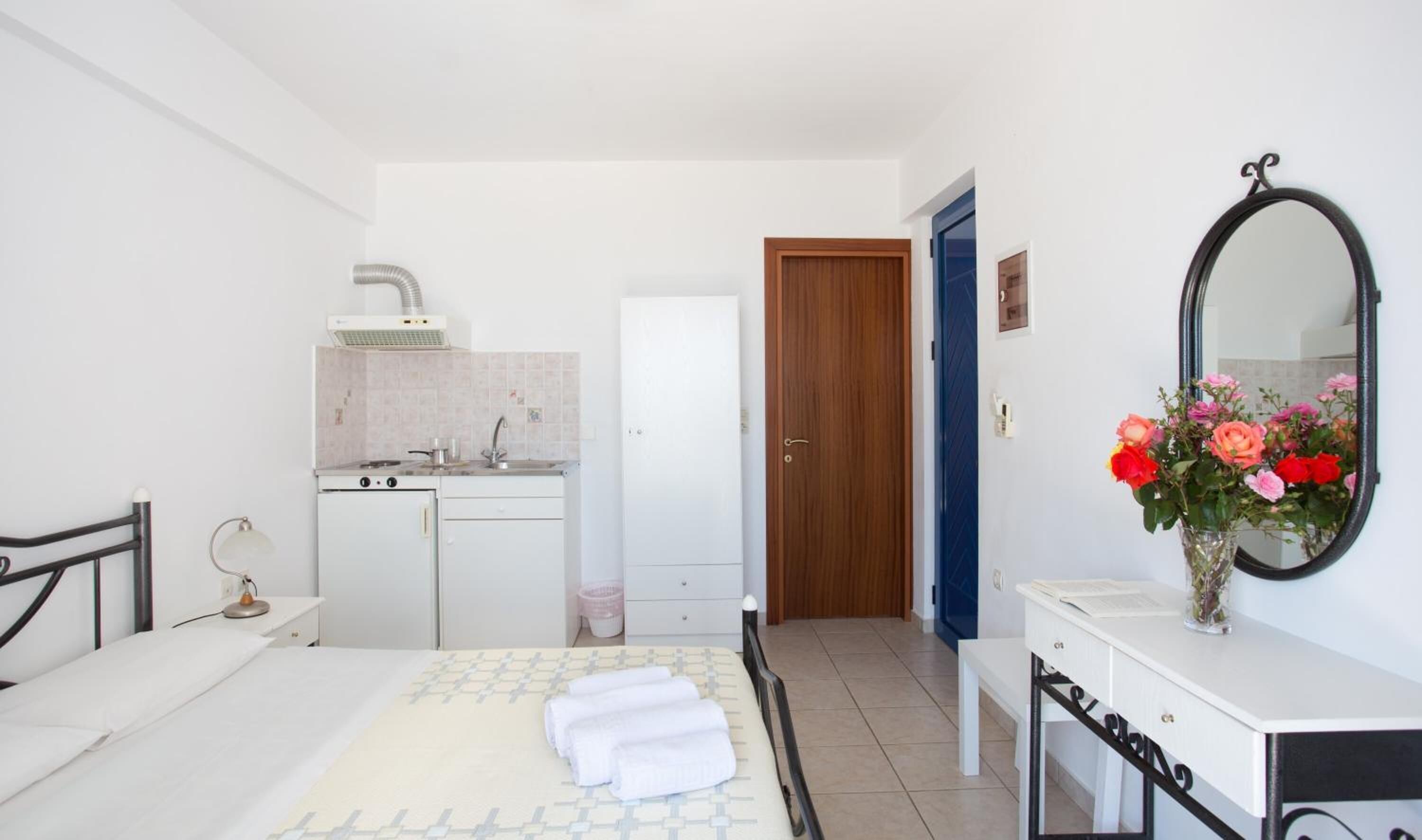 Une chambre à coucher comprenant un lit, une table de chevet, un miroir et une petite kitchenette équipée d’une cuisinière et d’un évier.