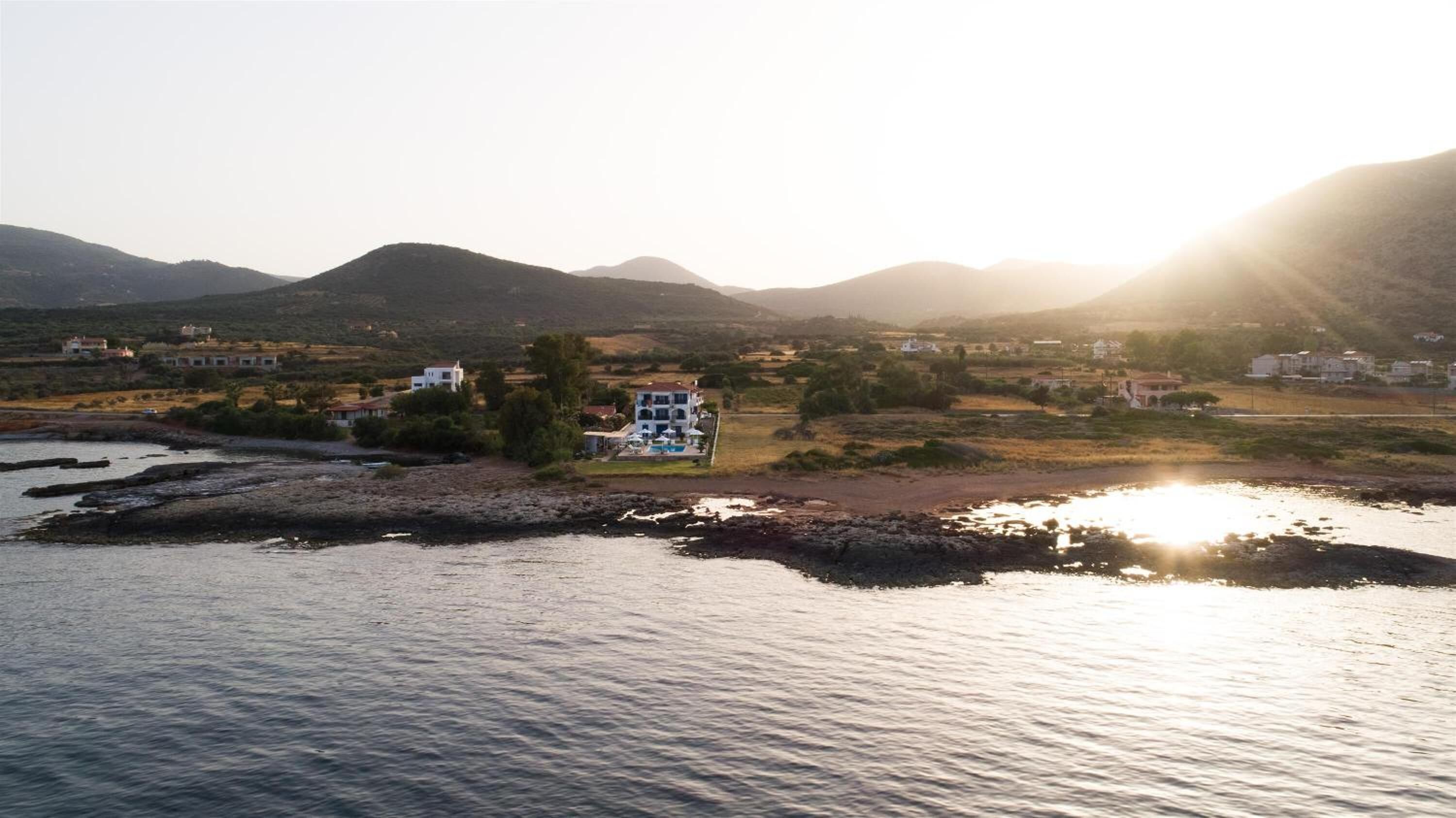 A coastal property with a large house, a swimming pool, and a view of the sea and mountains.