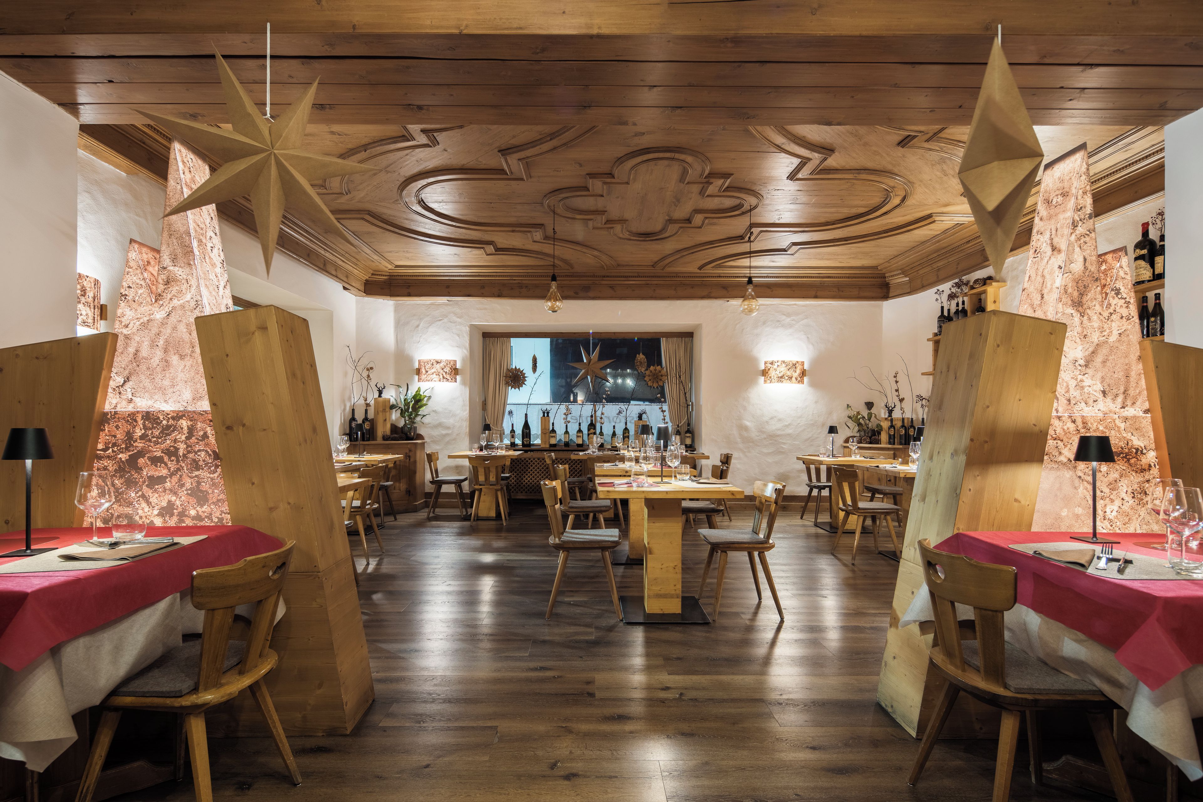 Interior de restaurante con mobiliario de madera, mesas preparadas para comer y una zona de bar con botellas.