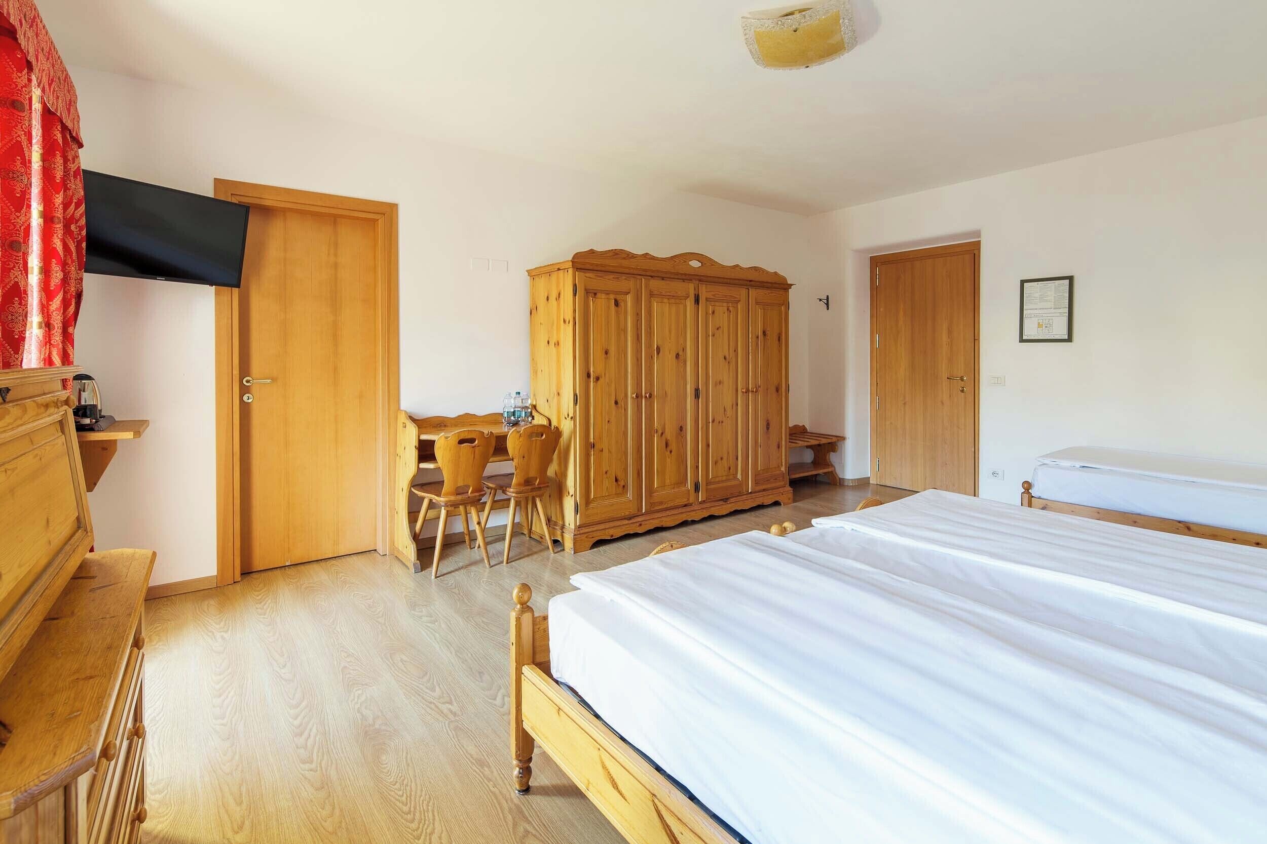 A bedroom with a wooden bed, a wardrobe, a desk with a chair, and a television mounted on the wall.