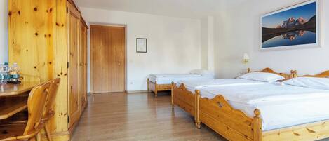 A room with a wooden bed, a wooden wardrobe, a desk with chairs, and a framed picture on the wall.