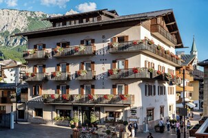 Un hotel de varios pisos con balcones decorados con flores, un paisaje montañoso al fondo y una torre del reloj.