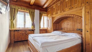Un dormitorio con suelo de madera, una cama, armario empotrado y ventana con cortinas.