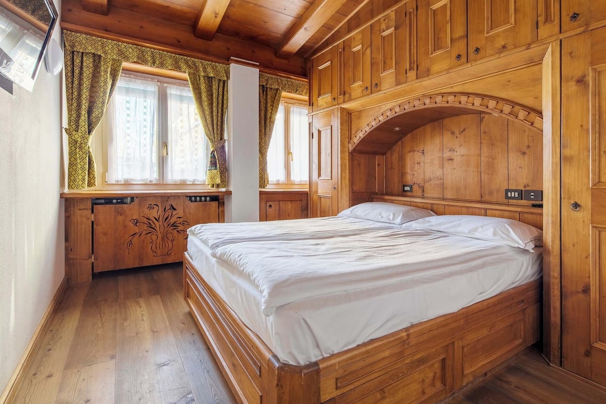 Un dormitorio con suelo de madera, una cama, armario empotrado y ventana con cortinas.