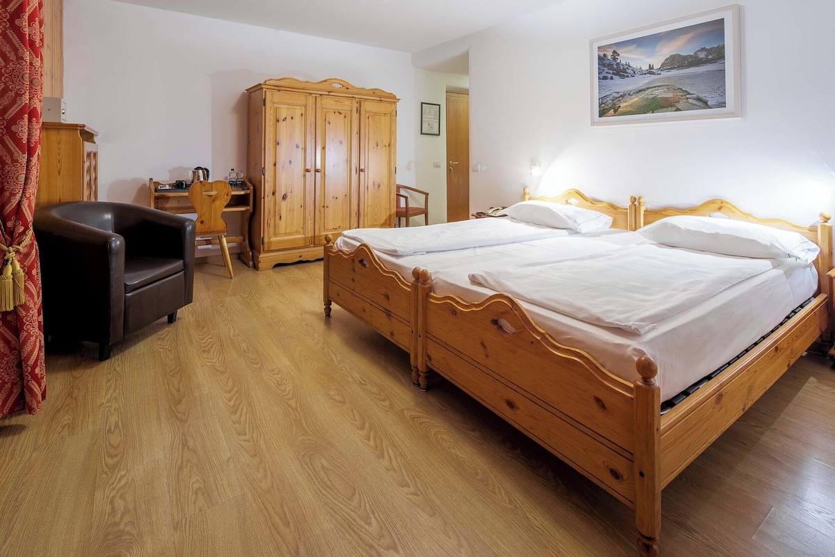 A bedroom with two wooden beds, a wooden wardrobe, a wooden desk, and a chair.