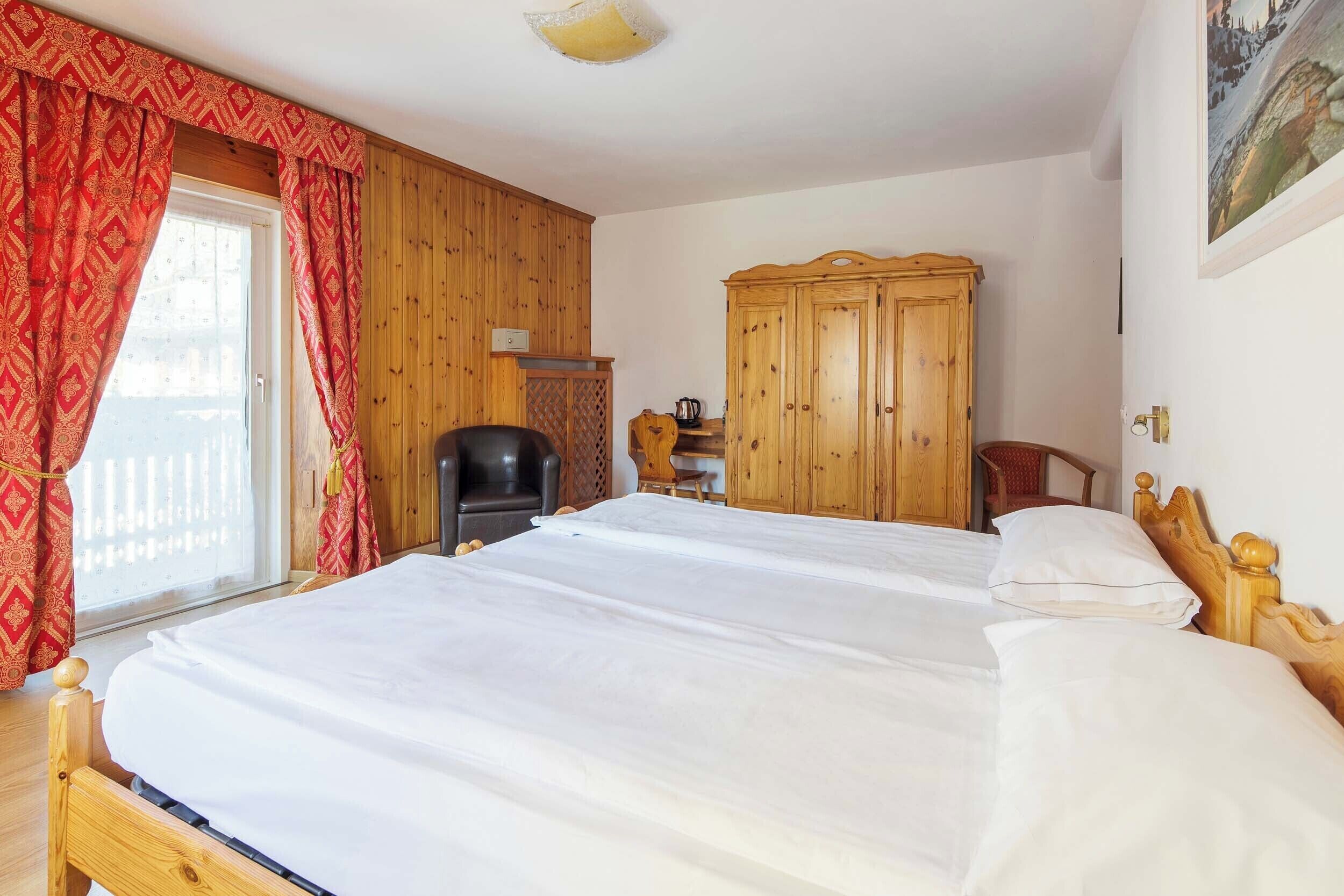 A bedroom with a large bed, wooden wardrobe, and a chair.