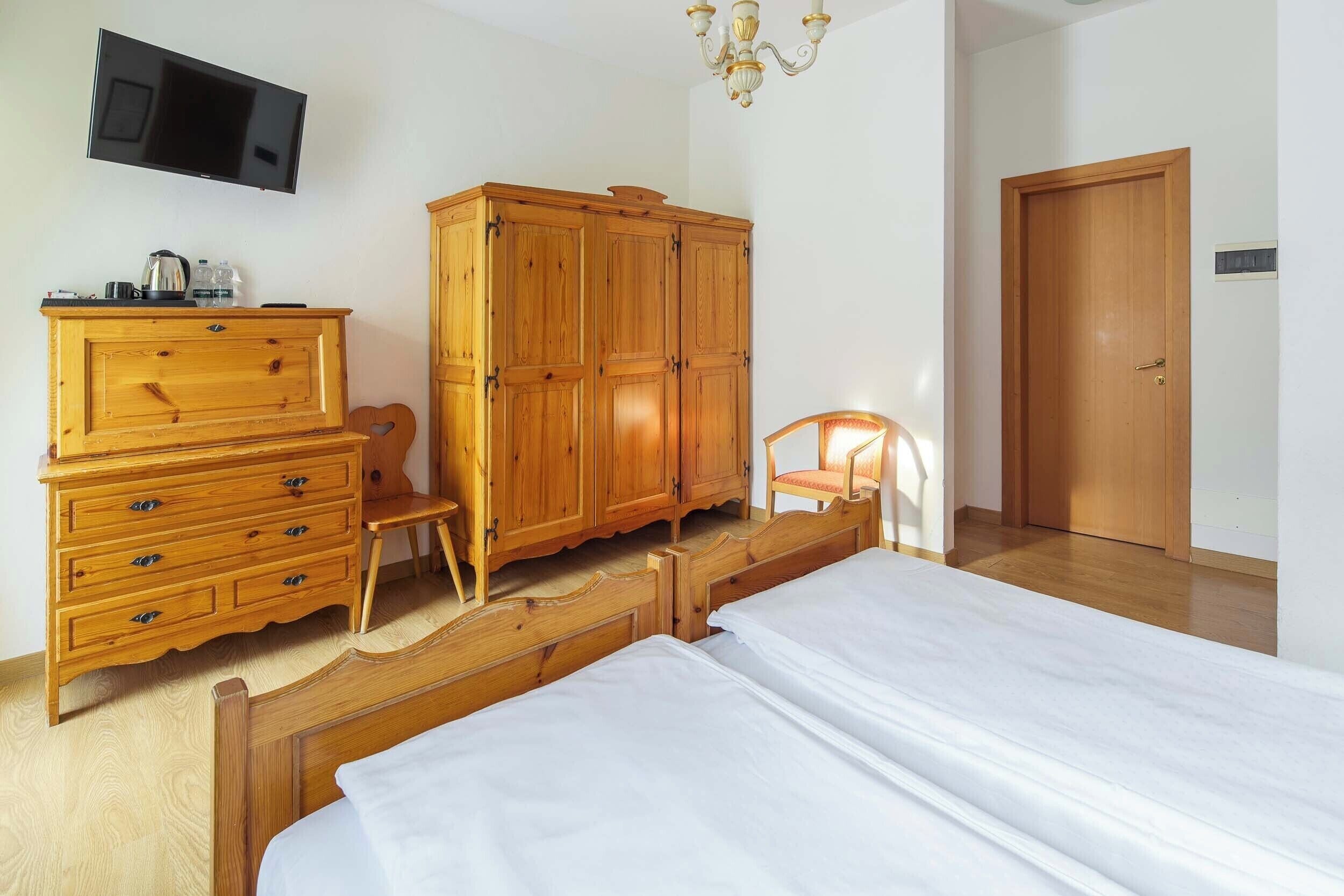 A bedroom with a bed, wooden wardrobe, a television, and a door.