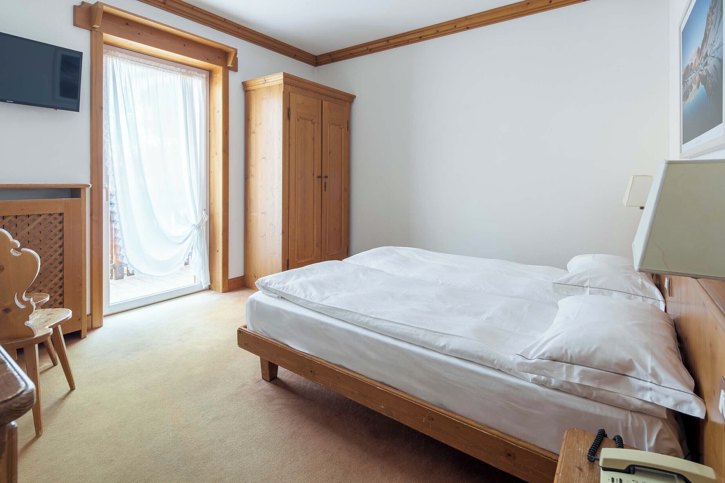 A bedroom with a wooden bed, a wardrobe, a desk, and a television.