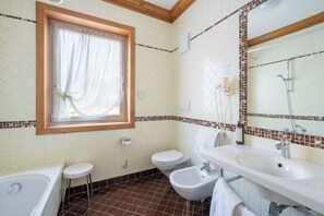 A bathroom with a bathtub, a bidet, a toilet, a sink, and a window with curtains. - Hotel Aquila (Cortina d'Ampezzo)