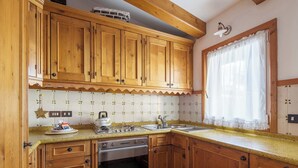 Una cocina con armarios de madera, horno empotrado, lavamanos y una ventana con cortina.