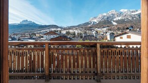 A balcony with a wooden railing overlooking a mountainous landscape with buildings and a ski slope. - Hotel Aquila (Cortina d'Ampezzo)