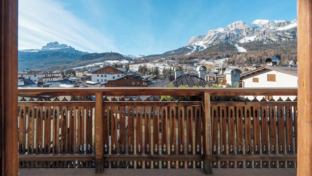 Un balcón con baranda de madera que da a un paisaje montañoso con edificios y una pista de esquí.