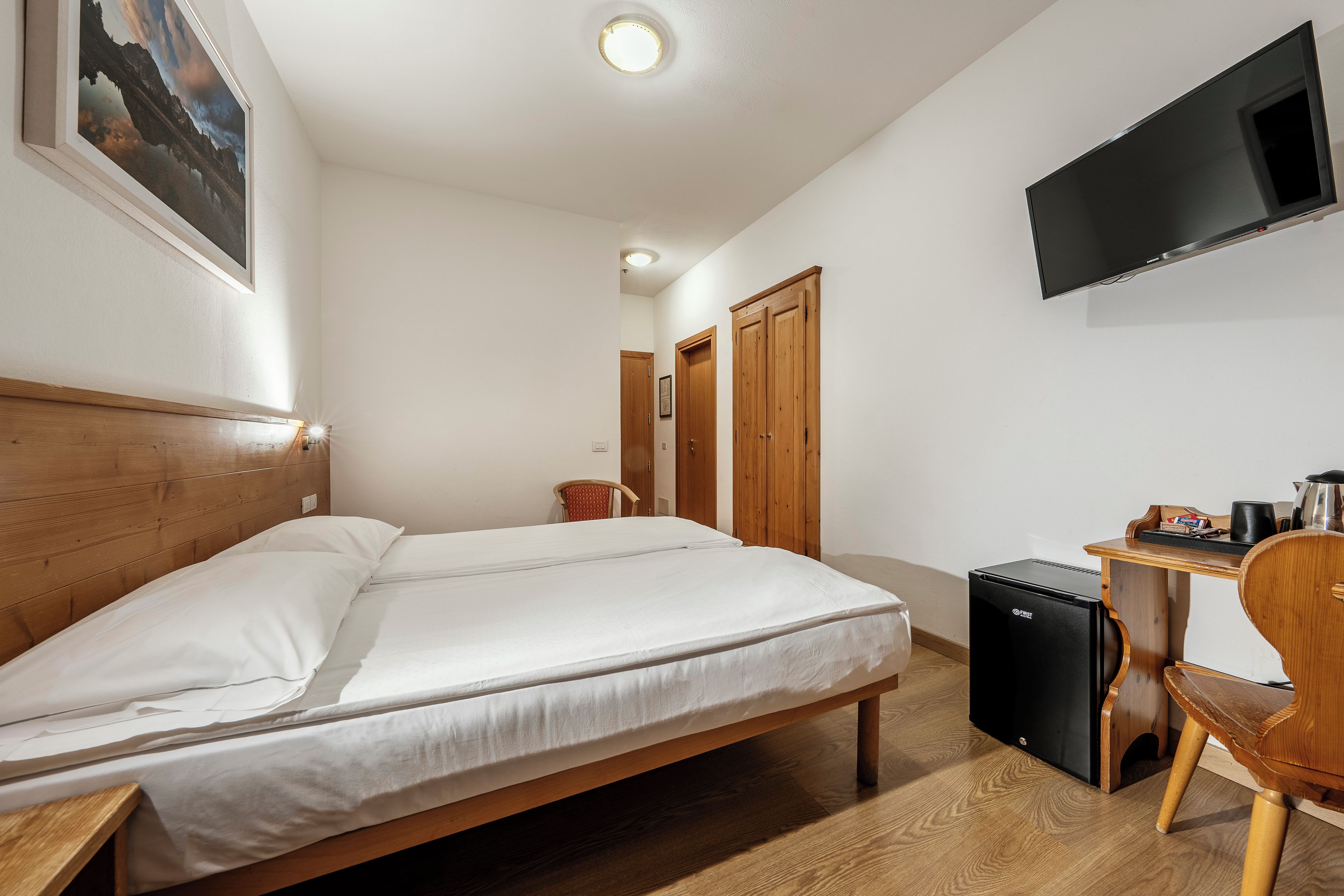 A hotel room with a bed, a desk, a chair, a television, and a small refrigerator.