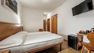 A hotel room with a bed, a desk, a chair, a television, and a small refrigerator.