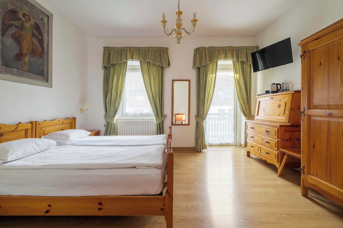 Una habitación de hotel con una cama de madera, un televisor, un aparador de madera y una araña.